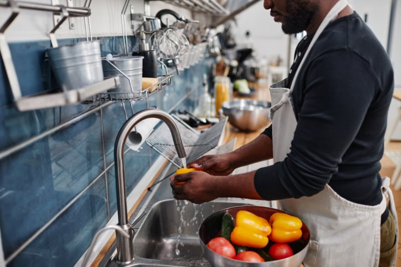 Side view portrait of African-American man washing fresh vegetables while cooking in kitchen, copy space.
